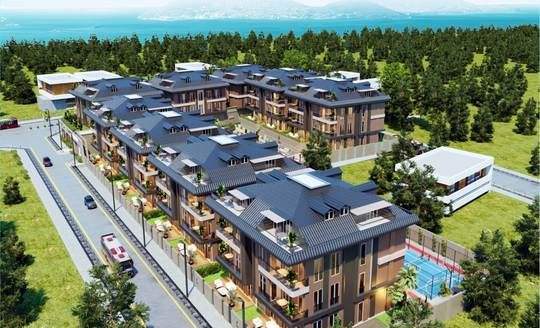 نمای هوایی از کل مجتمع مسکونی کم‌ارتفاع با سقف‌های شیروانی تیره، احاطه شده توسط درختان سبز و منظره دریا در دوردست، همراه با امکانات ورزشی