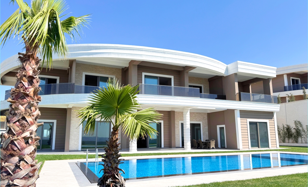 نمای بیرونی ویلای مدرن از سمت استخر، همراه با درختان نخل تزیینی و بالکن‌های بزرگ شیشه‌ای.
